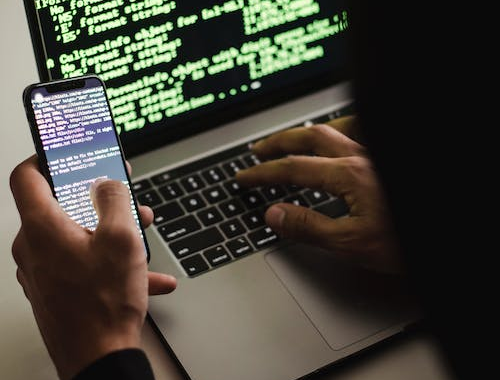 An image of a hacker with mobile coding on a laptop