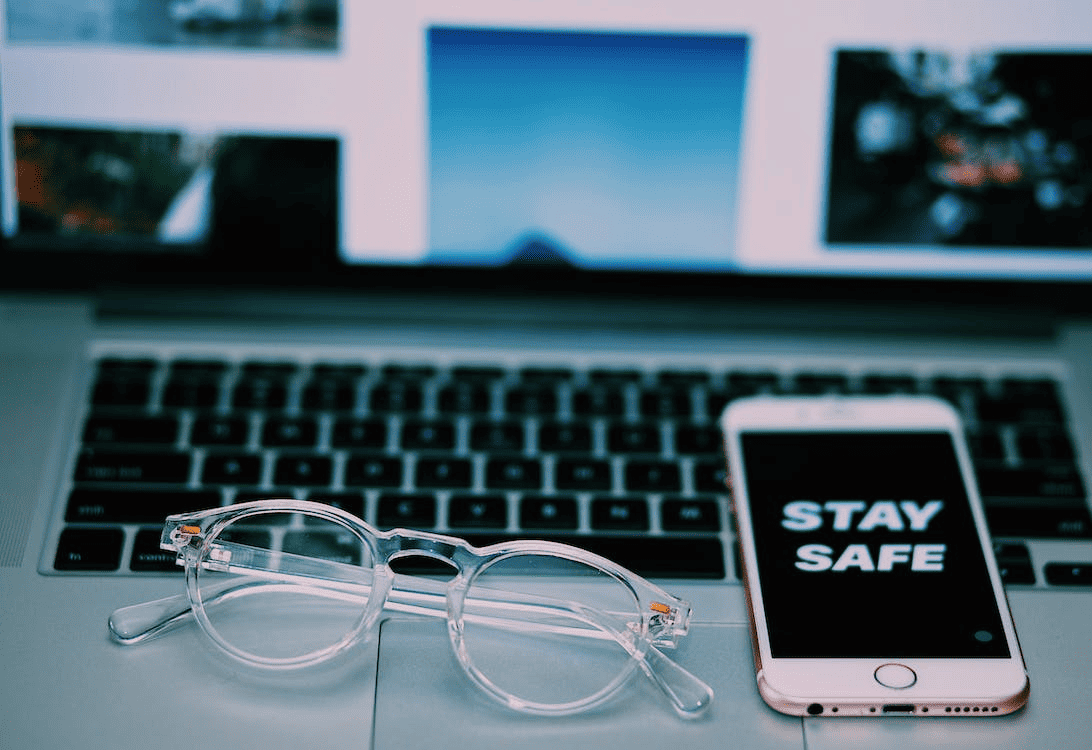 Stay safe” written on a mobile that is placed on a laptop along with spectacles