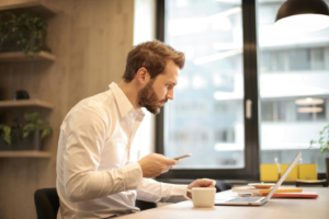 A man holding a cell phone is looking at a laptop