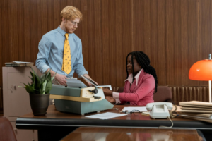 A man handing over documents to a woman in an office