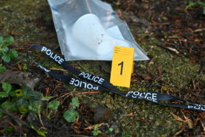 A piece of evidence in a sealed bag labeled with a marker, placed on the ground with a police tape nearby.