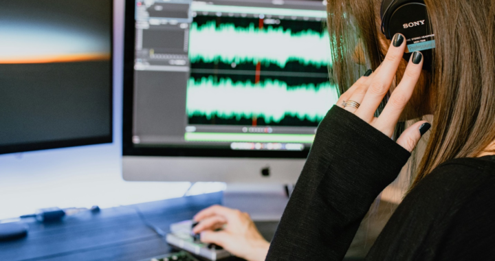 A forensic audio specialist wearing headphones and working on a computer with audio waveforms displayed on the screen, analyzing audio evidence for clarity and authenticity.