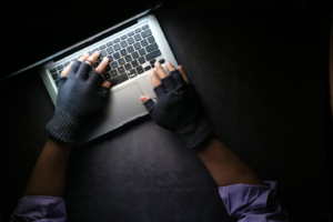 A forensic audio specialist wearing fingerless gloves working on a laptop, analyzing digital evidence for clarity and authenticity in a criminal investigation.