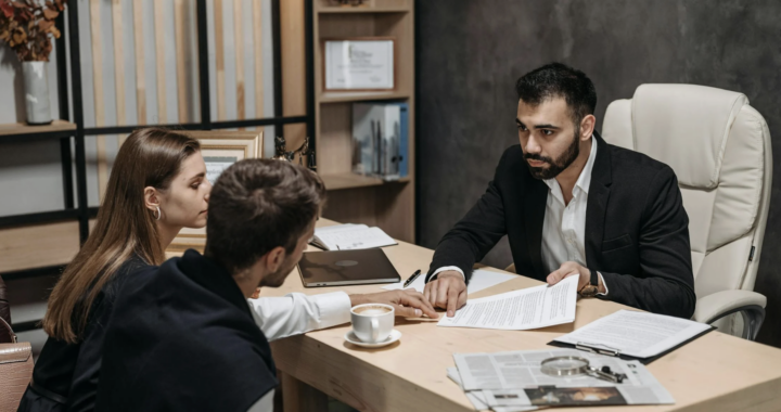 This photo shows a professional in business attire explaining documents across a desk.