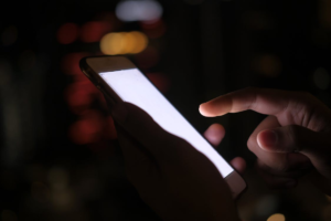 Hand using a smartphone with a bright screen in a dark room