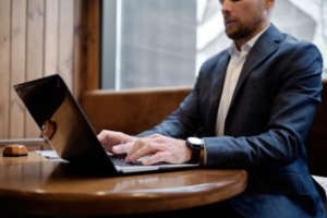Professional in a suit typing on a laptop at a wooden table.